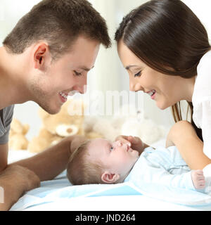 Des parents fiers de voir leur fils sur un lit à la maison Banque D'Images