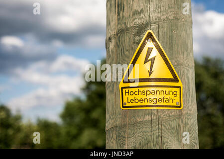 L'allemand signe haute tension monté sur poteau en bois avec l'arbre vert à l'arrière-plan Banque D'Images