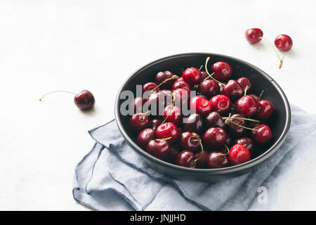 Les cerises dans un bol noir vue rapprochée. La récolte des petits fruits biologiques frais locaux Banque D'Images