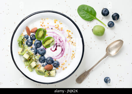 Le Yogourt aux bleuets, le kiwi, les épinards, les amandes, la noix de coco râpée et le pollen d'abeilles dans un bol sur le tableau blanc. Vue d'en haut Banque D'Images