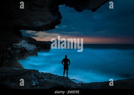 Un homme aime le coucher du soleil dans une caverne rocheuse en Crète avec de l'eau brute et de grosses vagues Banque D'Images