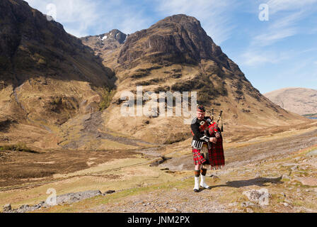 Un cornemuseur jouant de la cornemuse avec un fond de montagnes écossais Banque D'Images