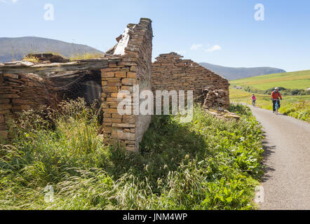 Deux cyclistes de remonter une colline passé un cottage en ruine, Hoy, Orkeny UK Banque D'Images