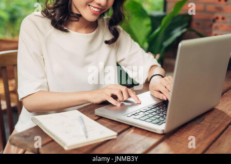 Young smiling woman sitting at table in cafe et écrit dans l'ordinateur portable Banque D'Images