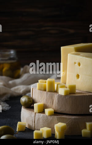 Disque suédois fromage jaune avec des trous sur les tranches de bois haché aux olives vertes sur fond rustique foncé Banque D'Images