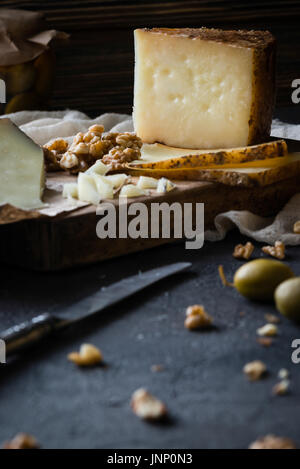 Assiette de fromage de manchego fromage espagnol haché et les tranches de Pecorino Toscano) Italien sur planche de bois, aux olives vertes dans un bocal en verre et noyer Banque D'Images