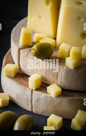 Close up of Swedish version fromage jaune avec des trous sur les tranches de bois haché aux olives vertes sur fond rustique foncé Banque D'Images