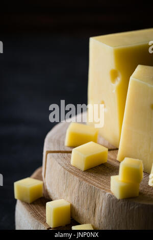 Gros plan du disque suédois fromage jaune avec des trous sur les tranches de bois haché sur fond rustique foncé Banque D'Images