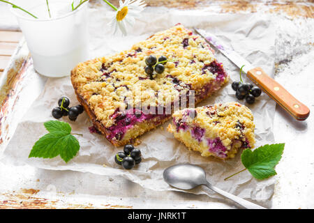 Le cassis et cottage gâteau crumble avec des feuilles vertes sur du papier sulfurisé et fond rustique Banque D'Images