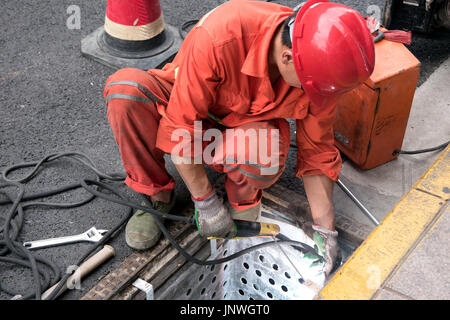 Travailleur utilise l'oxyde de fer à l'acier de l'électrode de soudure métallique du filtre de vidange des déchets d'égout à grille sur rue. Banque D'Images