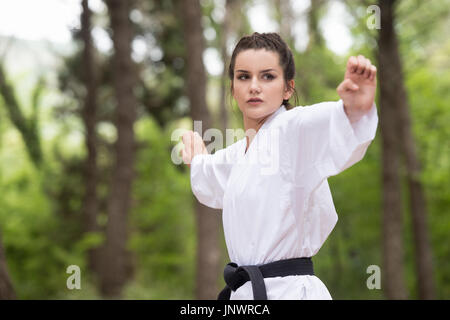 Jeune femme pratiquant des mouvements de karaté dans son bois de forêt - Kimono Blanc - Ceinture Noire Banque D'Images