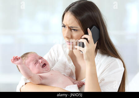 Mère appelant à un médecin sur le téléphone inquiète de son bébé pleurer désespérément à la maison Banque D'Images