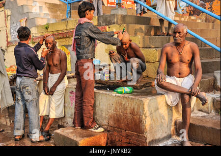 Un homme et un garçon ont leur raser la tête par les barbiers sur les ghats de Varanasi Banque D'Images