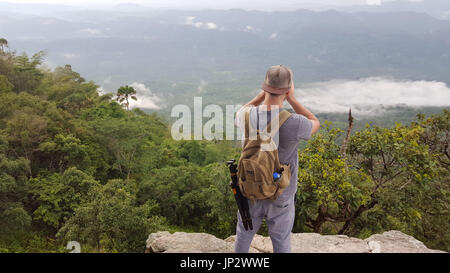 Photographe voyageur solo homme à prendre des photos d'une vallée brumeuse du bord d'une falaise dans la jungle sur la montagne. Banque D'Images