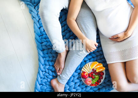 Jeune homme et femme enceinte assise avec plateau à fruits. La grossesse et la nutrition concept Banque D'Images