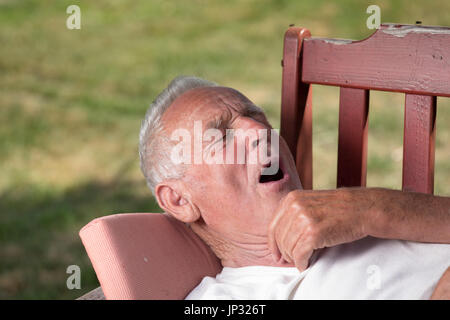 Hauts homme étendu sur un banc dans le jardin et somnolence. Le bâillement et la préparation pour siesta Banque D'Images