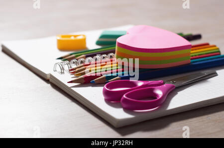 Close up of wooden des crayons et autres fournitures scolaires sur vide remarque livre sur un bureau en bois Banque D'Images