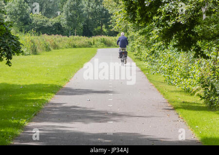 Vieil homme méconnaissable de faire du vélo sur route asphaltée. Banque D'Images