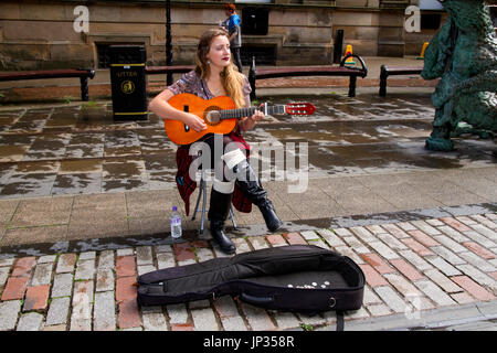 Un jeune élève musicien ambulant irlandais du sud jouant de la guitare et chanter pour gagner de l'argent sur un jour pluvieux à Dundee, Royaume-Uni Banque D'Images