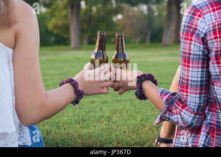 Amis féminins célébrant la maison de passer un bon moment de boire une bière dans un parc. Ils sont le grillage avec des bouteilles. Banque D'Images