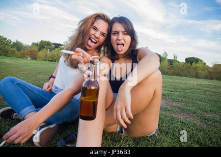 Deux filles, des amis, fumer des cigarettes et boire les bouteilles de bière dans le parc un jour nuageux. Ils sont de la fête et sont heureux. Banque D'Images