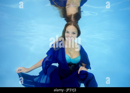 La femme en bleu dress posing sous l'eau dans la piscine Banque D'Images