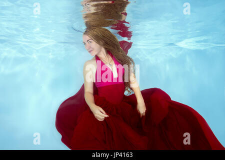 Jeune femme en robe rouge se faisant passer sous l'eau dans la piscine Banque D'Images