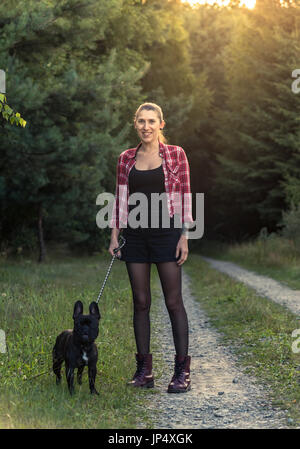 Hipster girl with tattoo balade Bouledogue Français en forêt. Effet Sun flare. Banque D'Images