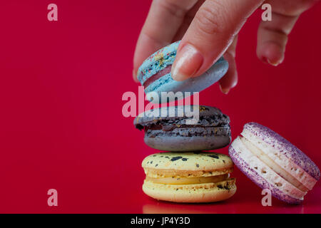 Beaucoup de macarons. Fond rouge. La main féminine prend un dessert Banque D'Images