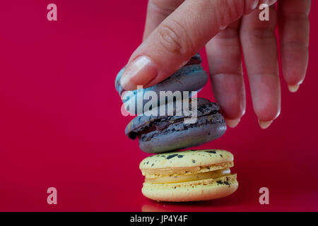 Beaucoup de macarons. Fond rouge. La main féminine prend un dessert Banque D'Images