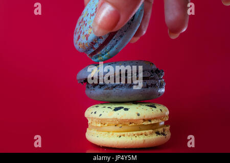 Beaucoup de macarons. Fond rouge. La main féminine prend un dessert Banque D'Images