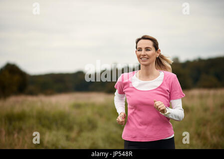 Cheerful woman running through field à l'automne, l'espace de copie vers la gauche Banque D'Images