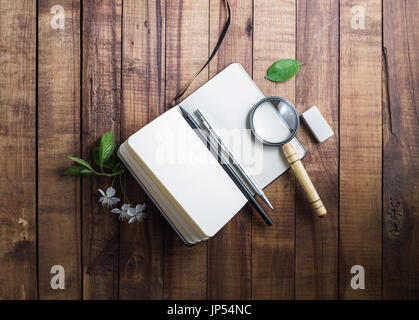 Photo de blank notepad, loupe, loupe, crayon, stylo, gomme, fleurs et feuilles vertes sur fond de bois. Modèle pour placer votre conception. St Banque D'Images