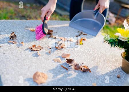 Une femme nettoie la tombe. Les socs à feuilles de la pierre tombale. Les préparatifs de la Toussaint le 1er novembre Banque D'Images