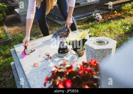 Une femme nettoie la tombe. Les socs à feuilles de la pierre tombale. Les préparatifs de la Toussaint le 1er novembre Banque D'Images