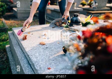 Une femme nettoie la tombe. Les socs à feuilles de la pierre tombale. Les préparatifs de la Toussaint le 1er novembre Banque D'Images