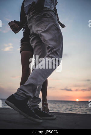 Low angle shot de deux personnes dansant sur un mur en face de la mer de l'océan. Banque D'Images