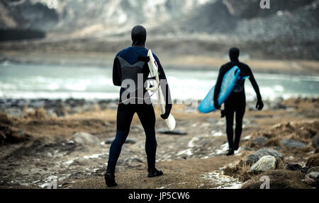 Deux surfeurs portant des combinaisons et l'exécution des planches à marcher vers l'océan avec des montagnes derrière.