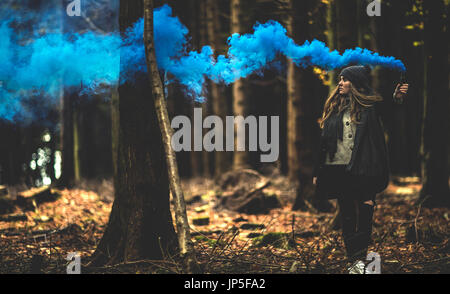 Une jeune femme qui traverse une forêt faisant une traînée de fumée bleue avec une torche de fumée. Banque D'Images