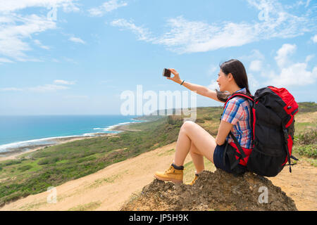 Tourisme backpacker selfies assis sur mountain heureux avec de beaux paysages en prenant des photos par mobile smartphone avec fond de l'océan du ciel. Banque D'Images