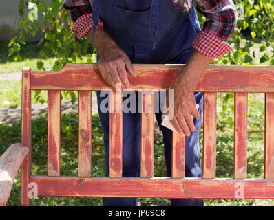 Man en salopette peinture vieux banc de jardin après sablage. La réparation de meubles anciens Banque D'Images