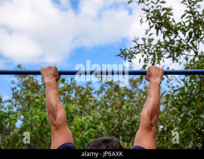 Les mains sur la barre de près. L'homme tire lui-même sur la barre. Faire du sport dans l'air frais. Barre horizontale Banque D'Images