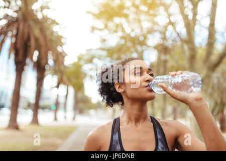 Woman runner eau potable d'une bouteille lors de l'entraînement. Athlète féminin de prendre une pause dans son entraînement. Banque D'Images