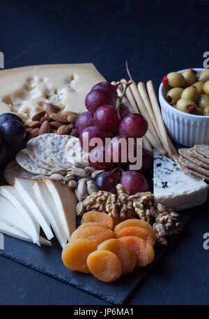 Assortiment de fromages, craquelins, raisins, noix et d'olive sur un fond noir Banque D'Images