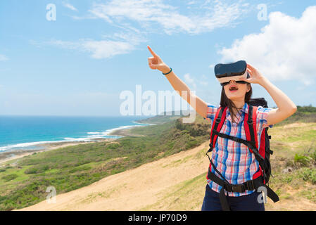 Chinois asiatique femme touristes détenteurs d'équipements de technologie le VR et pointant vers le blanc copyspace expérience 3D video lorsqu'elle a grimpé à la randonnée e Banque D'Images