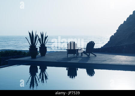 Deux chaises de détente en bois à côté d'une piscine donnant sur la mer. Banque D'Images