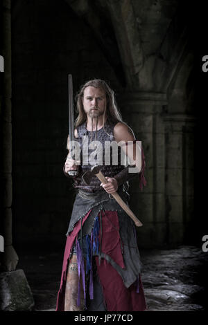 La reconstitution médiévale viking warrior soldat, jeune homme avec de longs cheveux tressés, barbe et portant des tatouages viking Banque D'Images