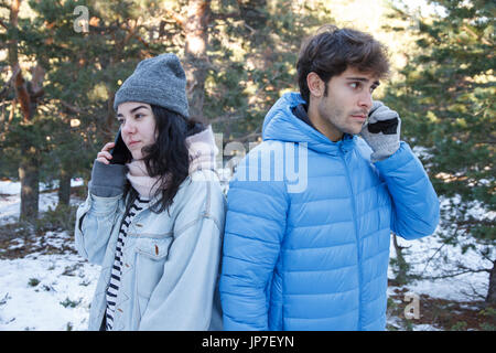 Petit ami et petite amie couple sont parler au téléphone pendant qu'ils sont sur une date dans les montagnes sur un jour de neige. Ils s'ennuient. Banque D'Images