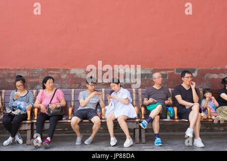 Les touristes chinois de différents âges assis sur un banc à la Cité interdite à Pékin - certains de manger certains sur leurs téléphones cellulaires et assis Banque D'Images