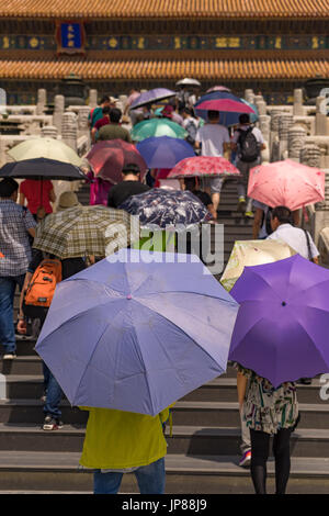 Les touristes détenteurs de parasols colorés de grimper les escaliers à la salle de l'harmonie suprême dans la Cité Interdite, Pékin, Chine